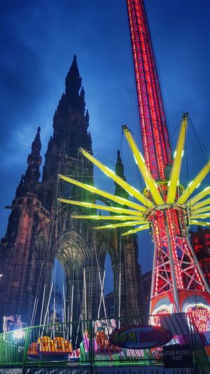 Low angle view of chain swing ride and scott monument against sky at dusk