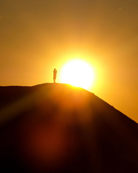 Silhouette person standing on orange sun against sky during sunset