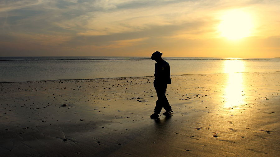 Man walking at beach against sky during sunset