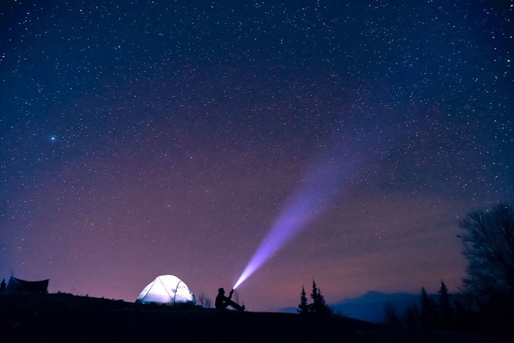 Silhouette man flashing light in sky at night
