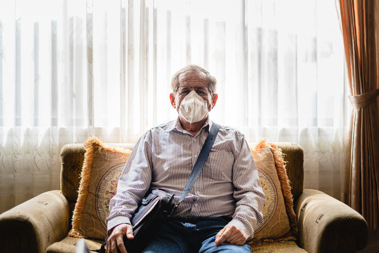 Senior man wearing mask sitting on sofa at home