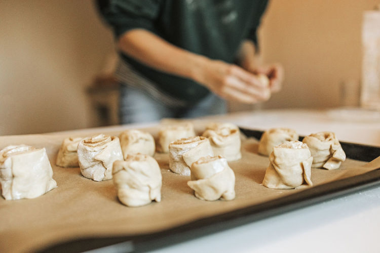 Arranged cinnamon rolls on baking sheet while woman in background at kitchen