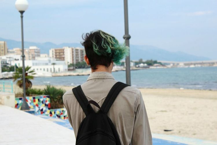 Rear view of man with green hair at beach against sky