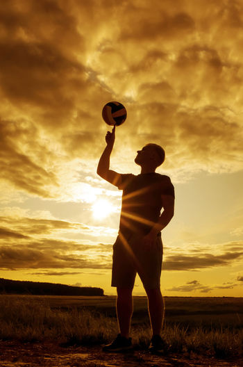 Rear view of silhouette man playing on field against sky during sunset