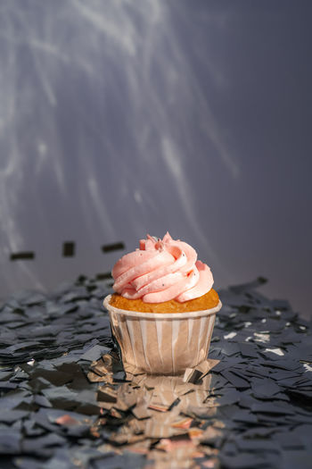 A cupcake with a pink cap stands among the flying silver confetti.
