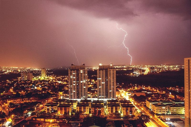 Illuminated cityscape against thunderstorm in sky at night