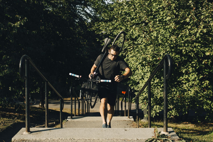 Active male athlete climbing steps while carrying bicycle in park