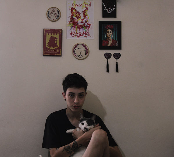 Portrait of woman with cat sitting by wall at home