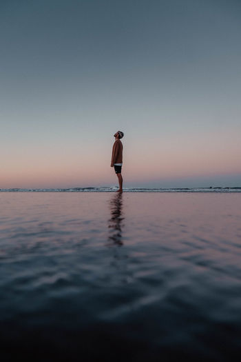 Man standing in sea against clear sky during sunset