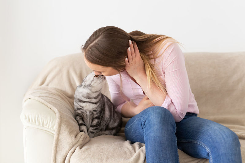 Woman kissing cat while sitting on sofa at home