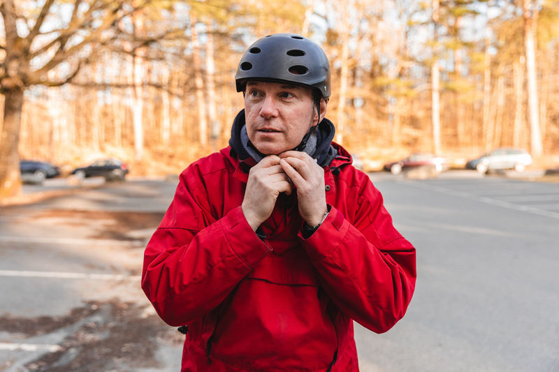 Adult male putting on protective helmet while standing in park in autumn during weekend