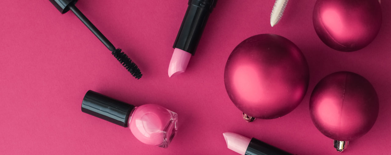 Close-up of christmas ornaments with beauty products on pink background
