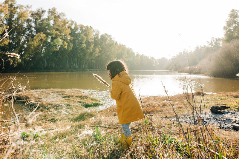 Full length of girl holding cattail standing by river