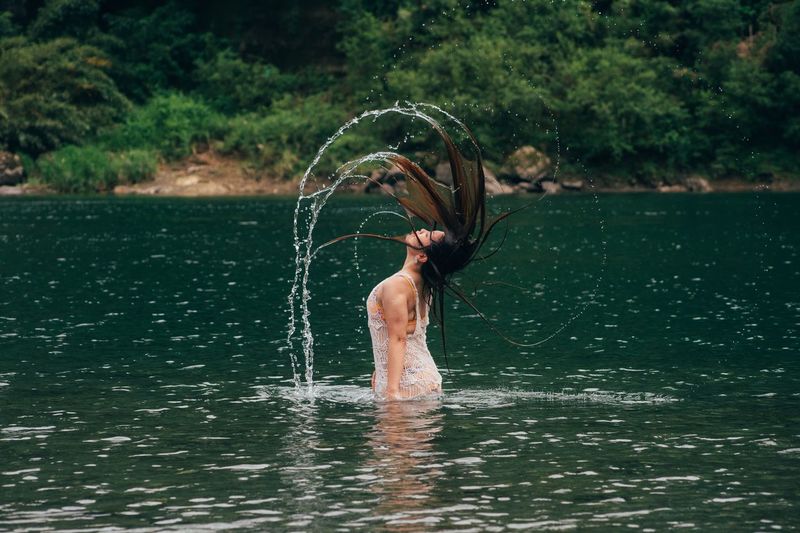 Side view of woman tossing hair while standing in river