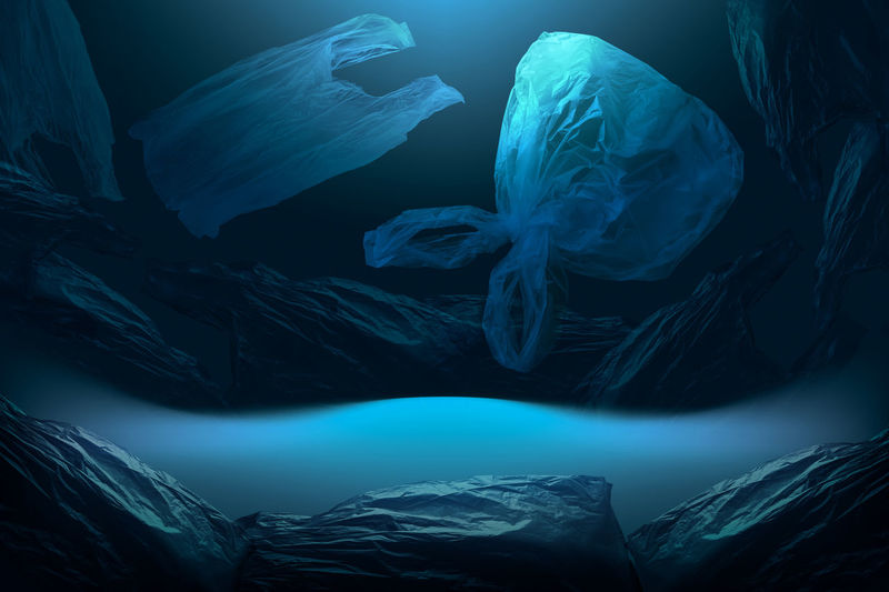 Creative background of single-use plastic bags floating in deep blue sea or ocean