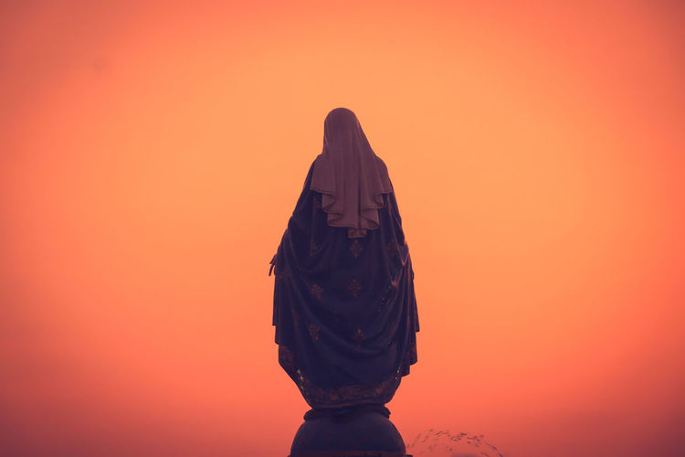 Rear view of woman standing against orange sky