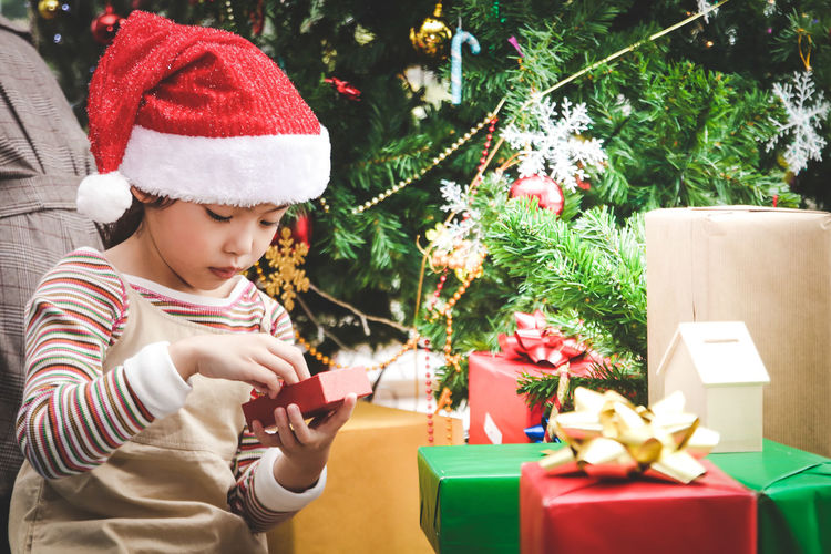 Girl wearing santa hat sitting with gifts against christmas tree