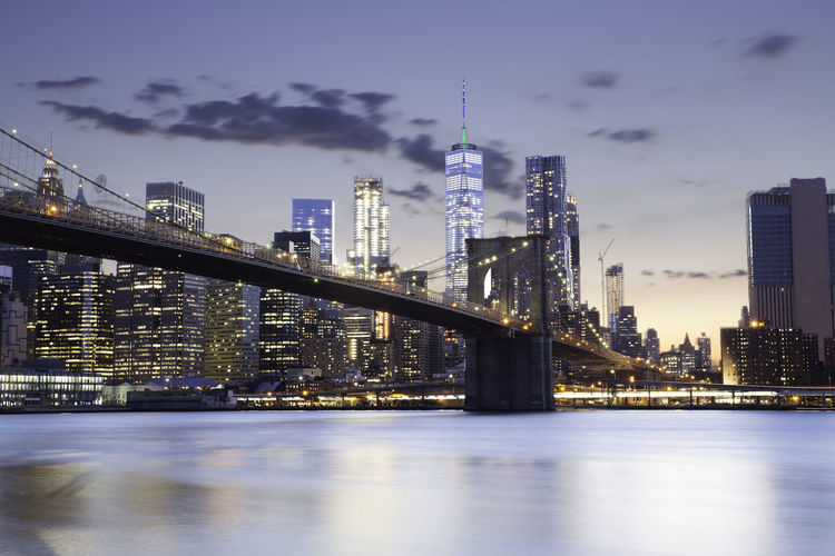 Brooklyn bridge over east river against illuminated modern buildings