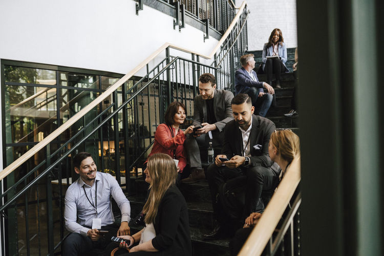 Businessmen and businesswomen discussing while sitting on staircase during networking event