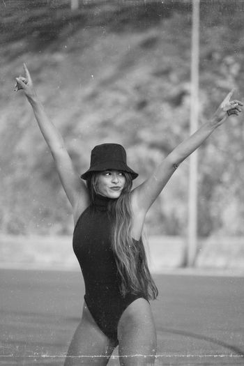 Beautiful young woman with arms raised standing on road