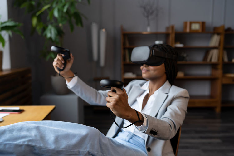 Smiling african american woman in vr glasses playing virtual reality games during work break