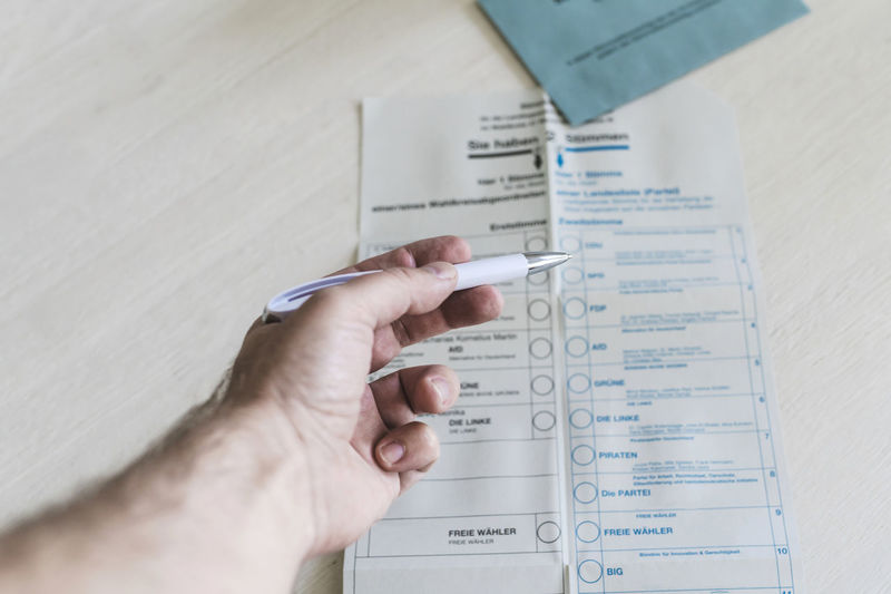Man holding ballpoint pen over ballot paper on table