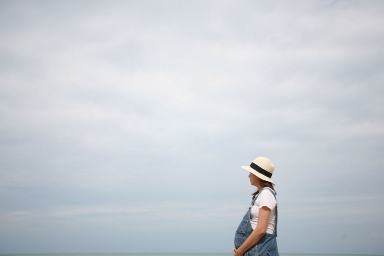 Side view of pregnant women standing against sky