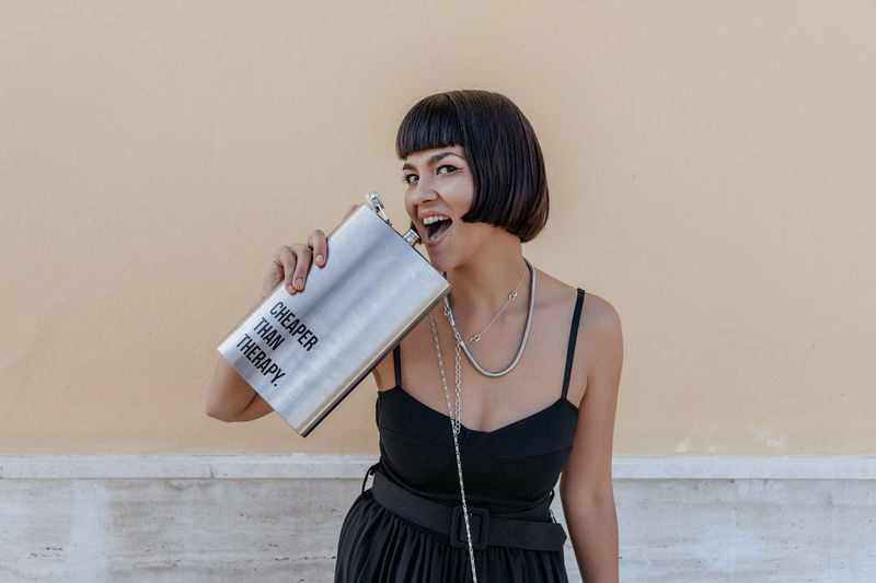 Portrait of happy young woman wearing elegant black jumpsuit, holding large liquor flask