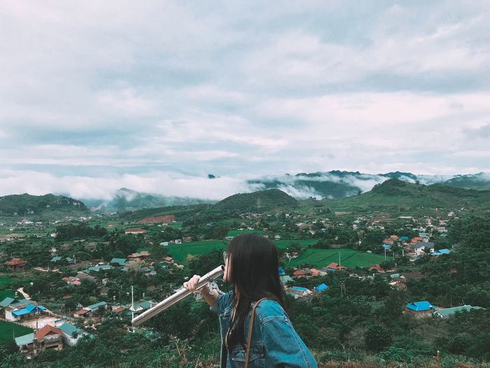 Side view of woman holding pipe with landscape in background against cloudy sky