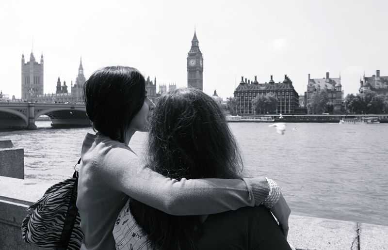 Mother and daughter by thames river against big ben on sunny day
