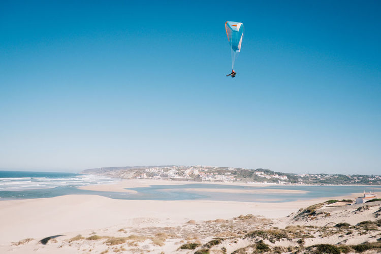 Person paragliding over sea against clear blue sky