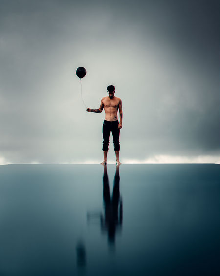 Man holding ball while standing in sea against sky