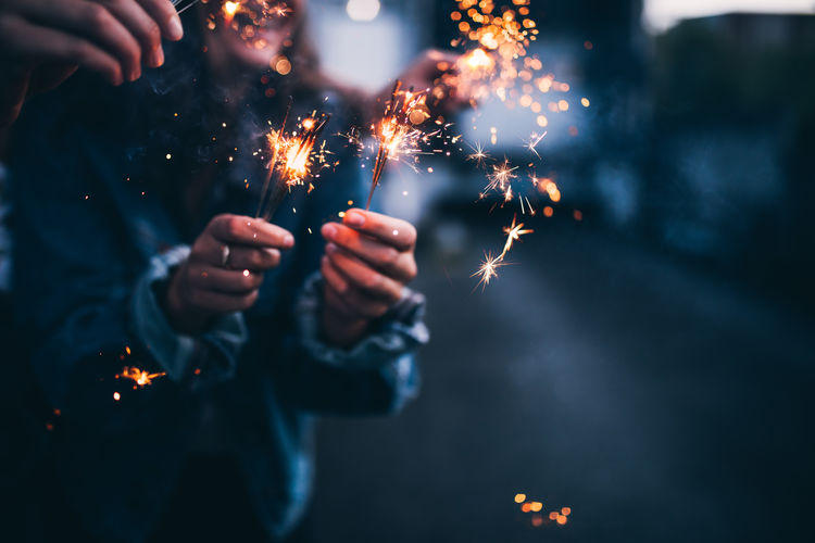 Close-up of person holding sparkler against illuminated background