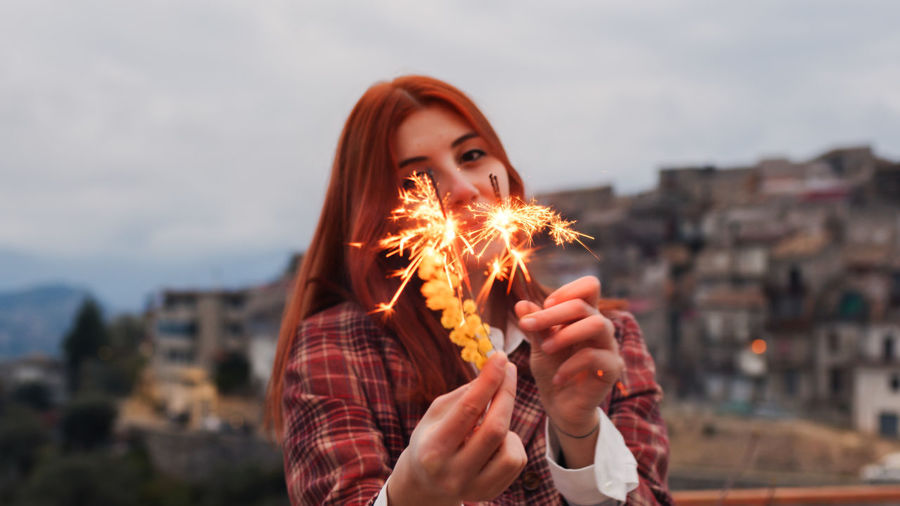 Cropped hand of woman holding sparkler against sky