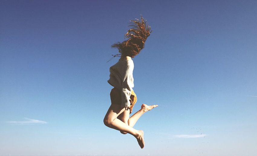 Full length of young woman tossing hair in mid-air against clear blue sky