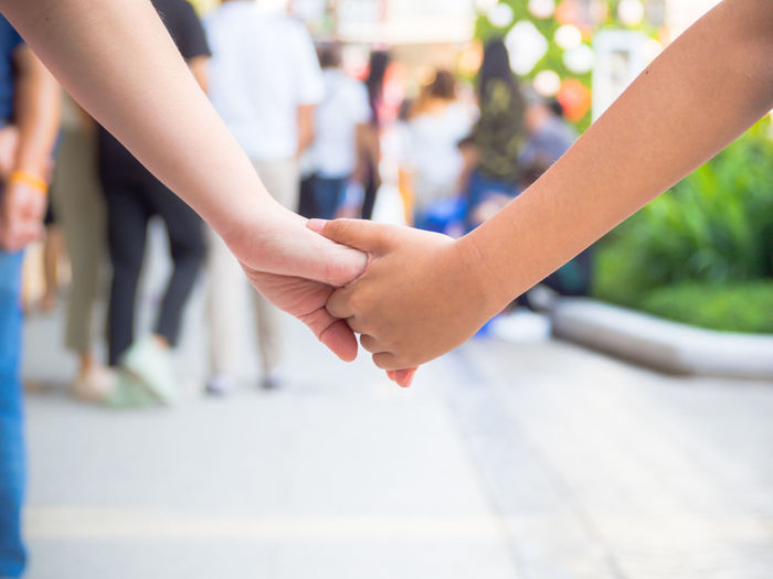 Cropped image of mother and daughter holding hands while walking on street