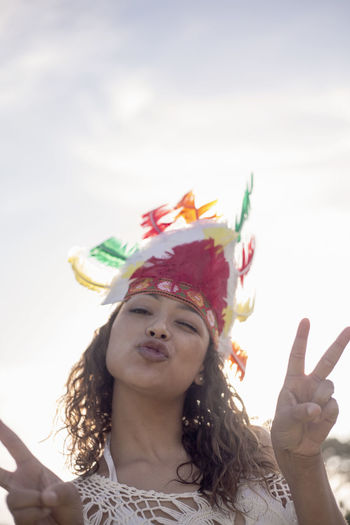 Woman wearing native american headdress showing hand sign while standing against clear sky