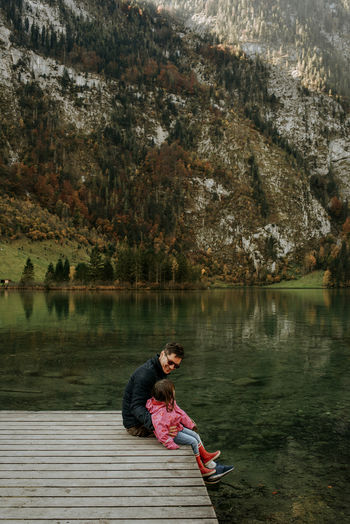 Side view of father and daughter sitting by lake