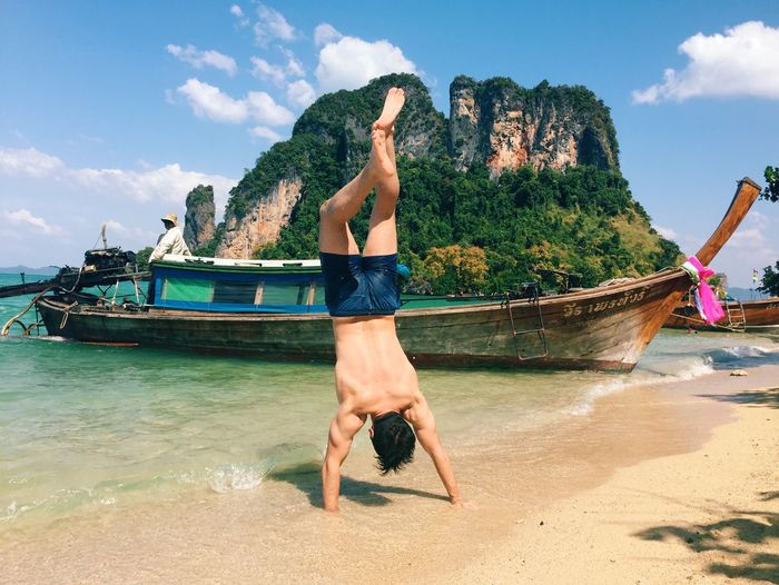Rear view of man performing handstand at sea shore