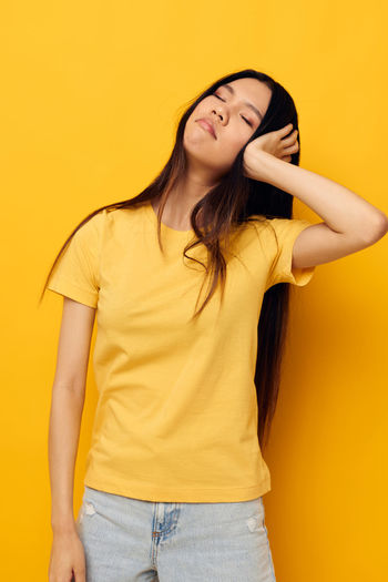 Portrait of young woman standing against yellow background