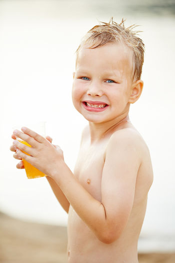 Portrait of wet smiling boy with orange juice standing at beach