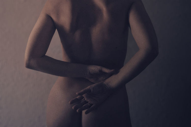 Midsection of naked woman standing by wall