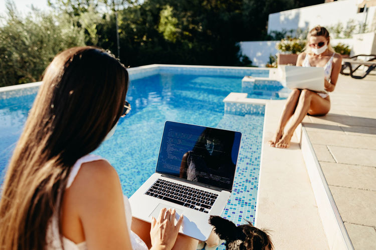 Rear view of woman using laptop sitting by swimming pool