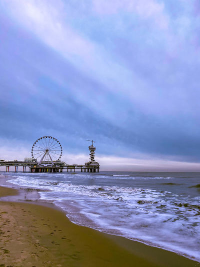 Ferris wheel at beach against cloudy sky