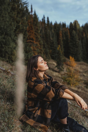 Young woman looking away while sitting on land in forest