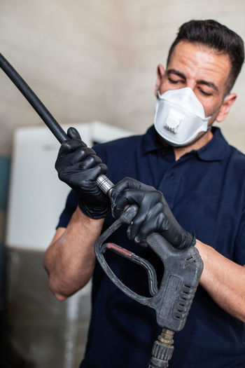 Adult man in respirator and latex gloves attaching nozzle to hose while working in garage