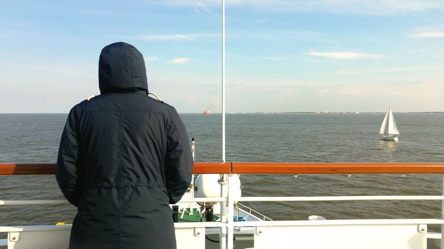 Rear view of man standing on railing against sea