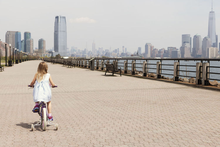 Rear view of girl cycling on promenade with city skyline in background