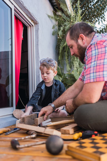 Ground level of cheerful bearded dad in checkered shirt with boy working with wooden blocks
