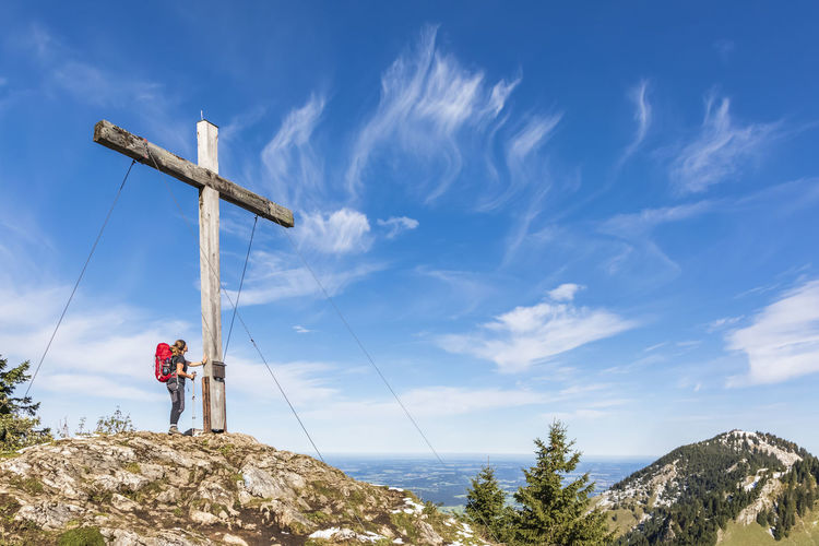 Germany, bavaria, female hiker standing in front of summit cross of karkopf mountain